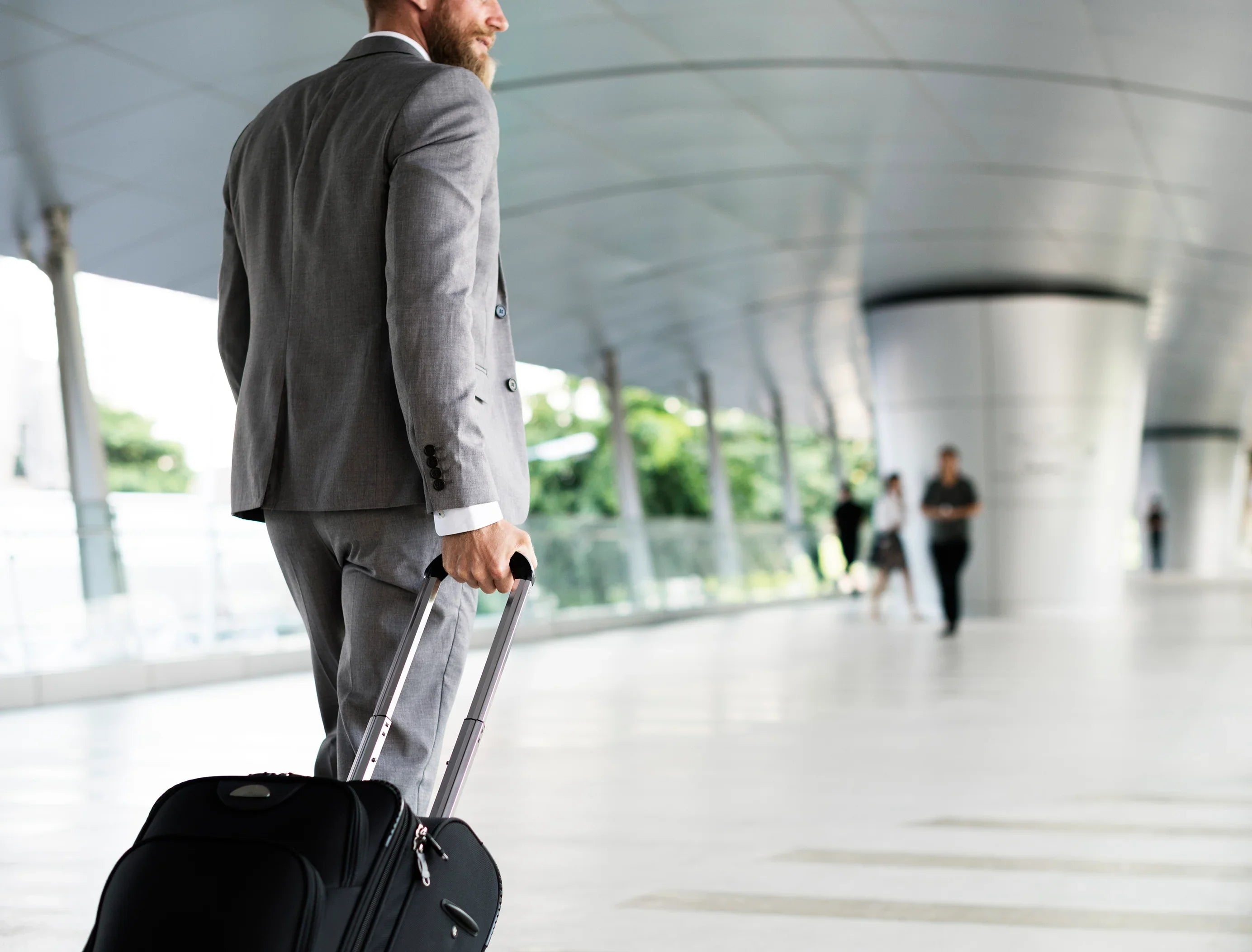 Businessman in grey suit pulling suitcase in modern indoor walkway