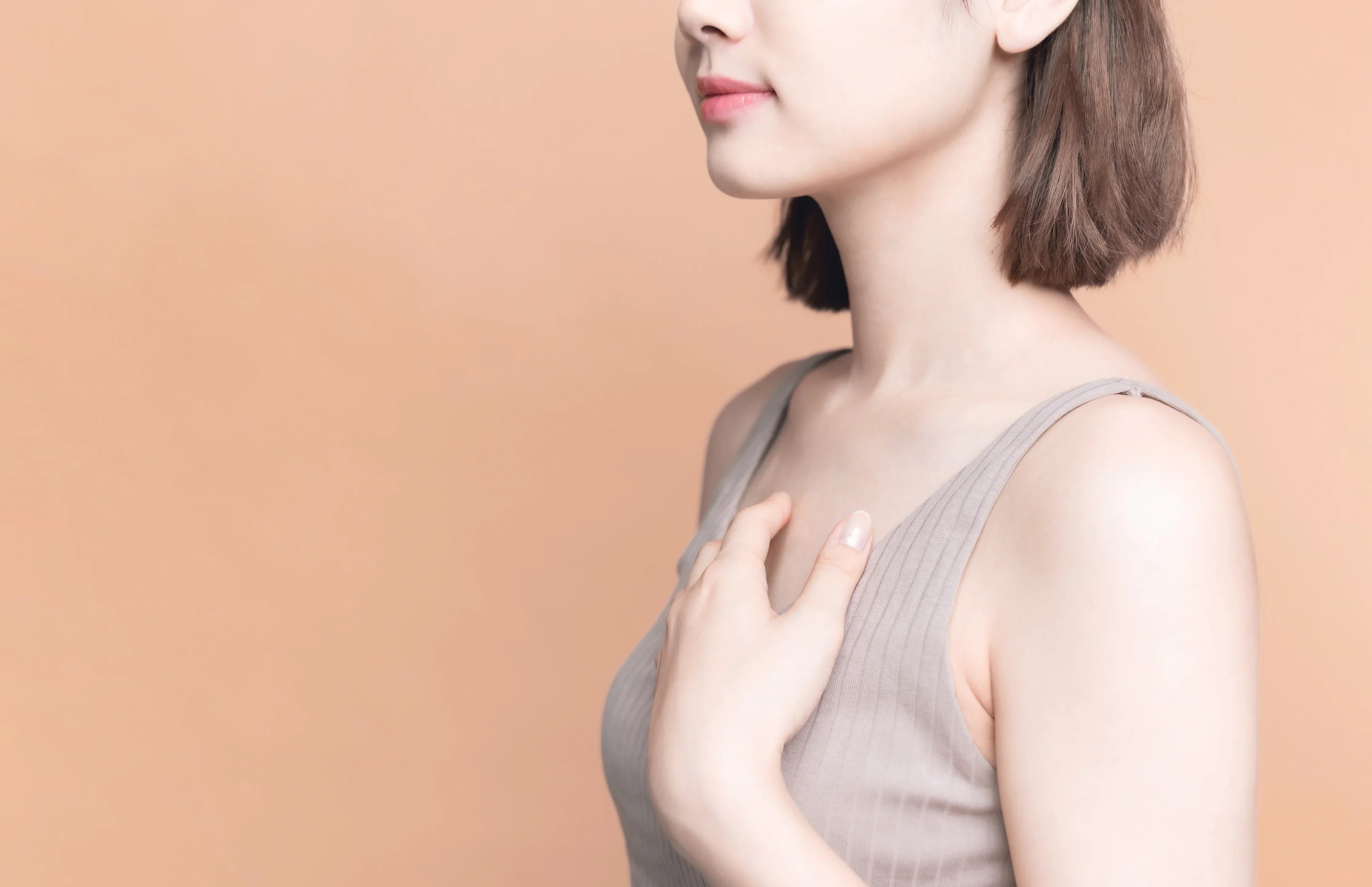 Woman wearing a hypoallergenic cotton tank top touching her chest, neutral peach background