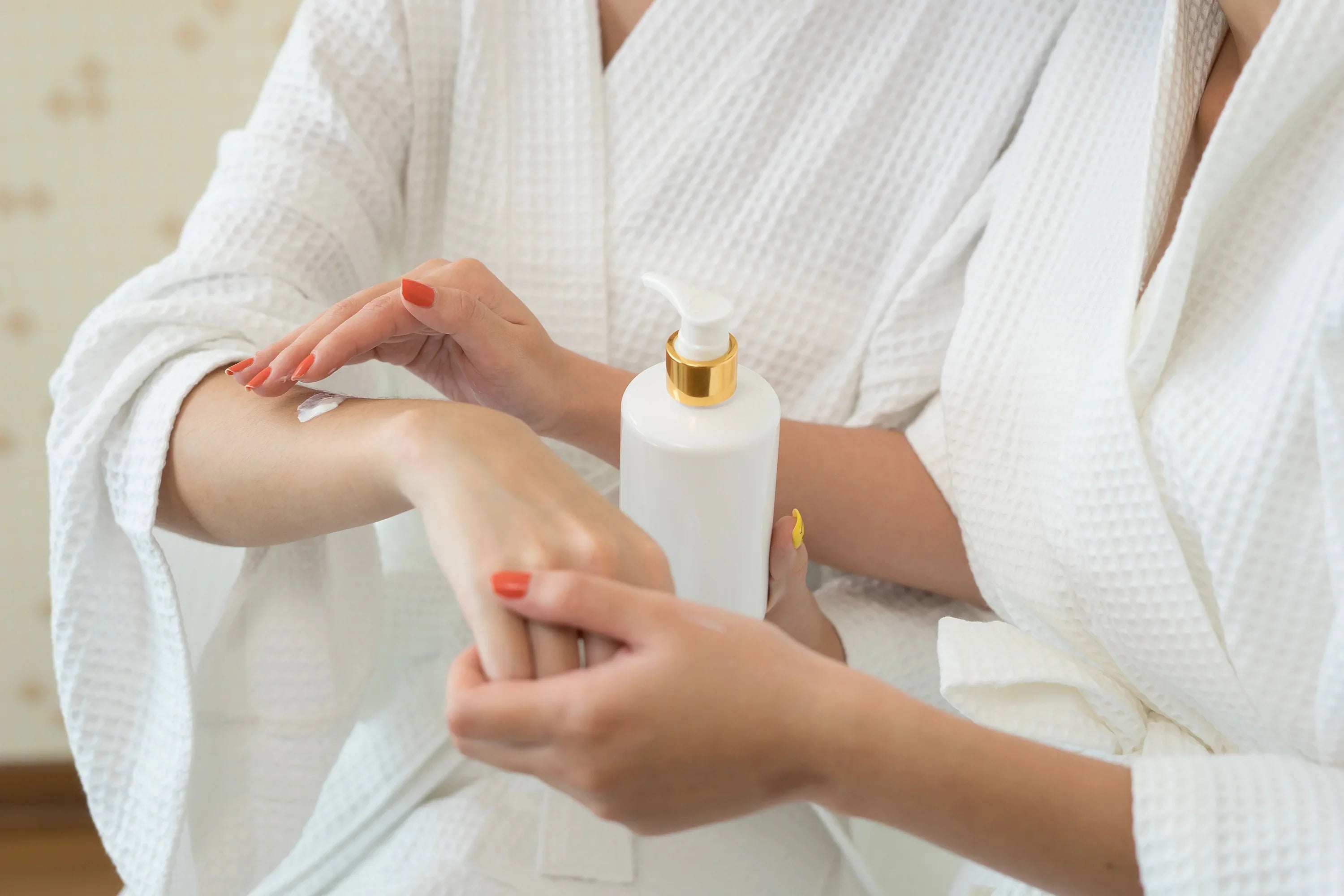 Two women in white bathrobes applying moisturizer to hand, skincare for sensitive skin