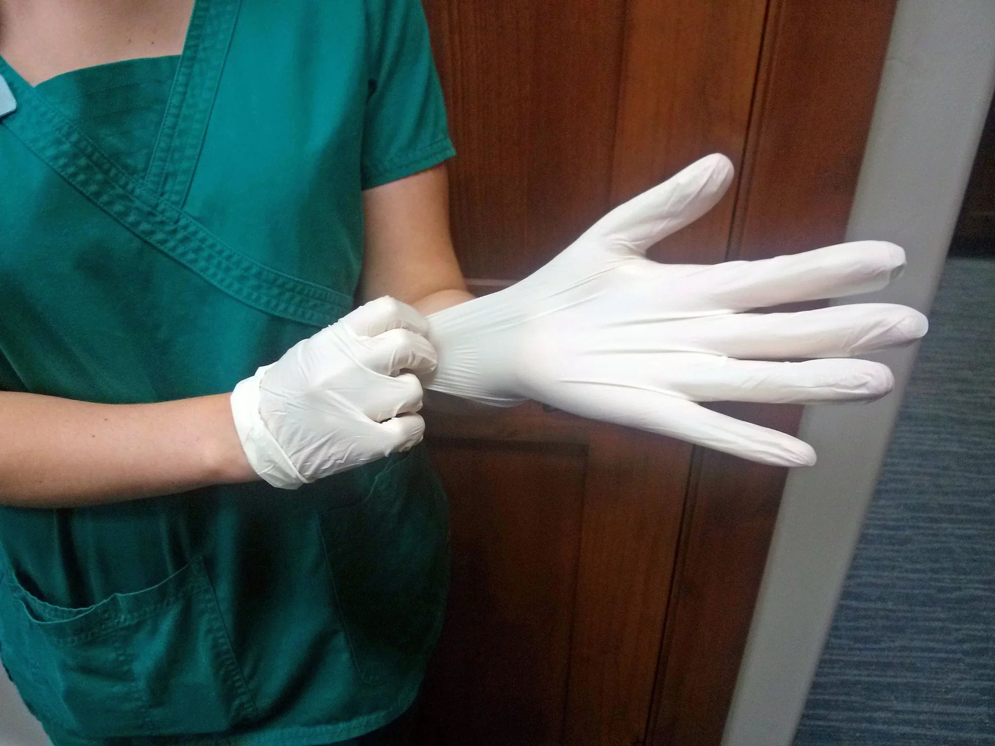 Person in green medical scrubs putting on white latex gloves, allergy awareness