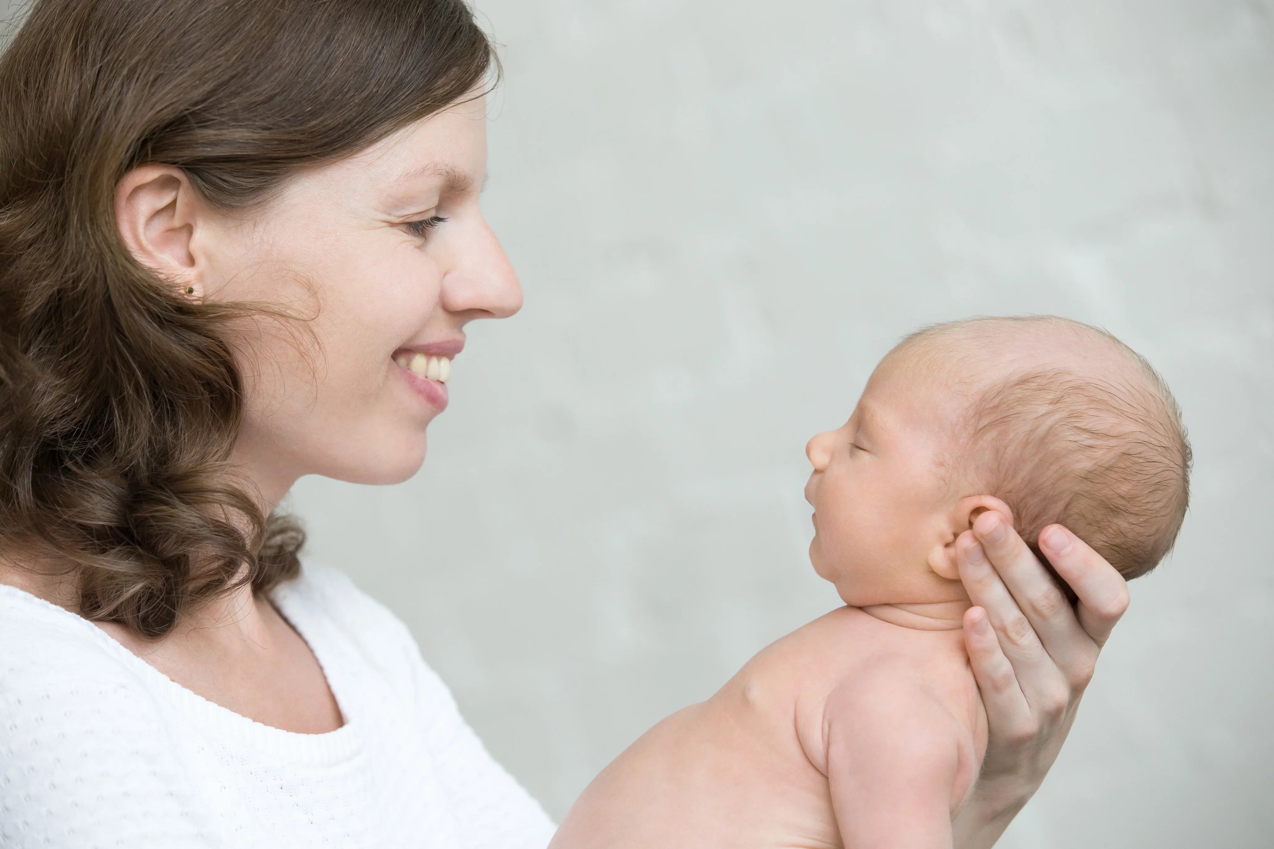 Smiling woman in white holding newborn, promoting hypoallergenic cotton clothing