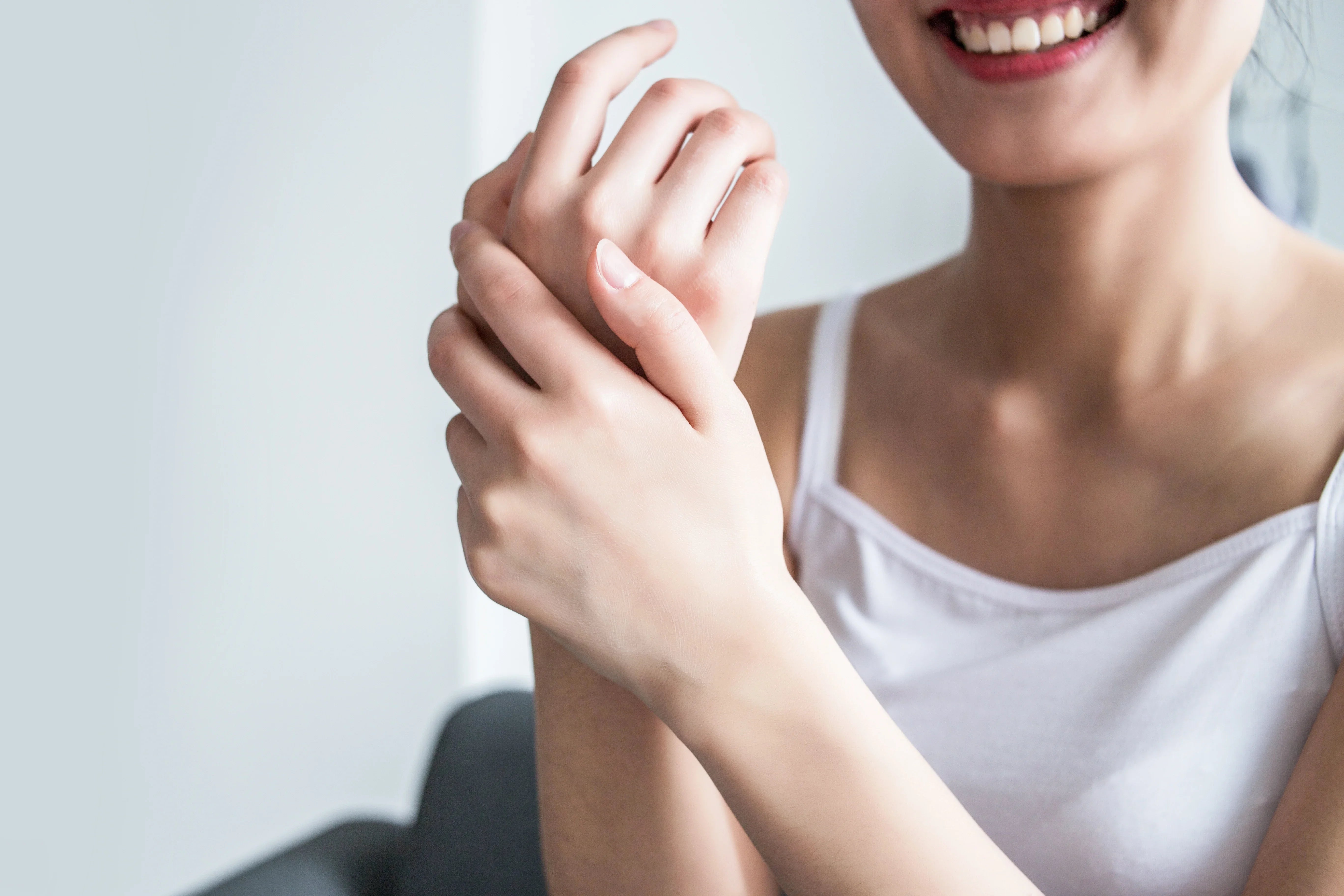Smiling woman in white tank top applying cream to hands, ideal for sensitive skin care