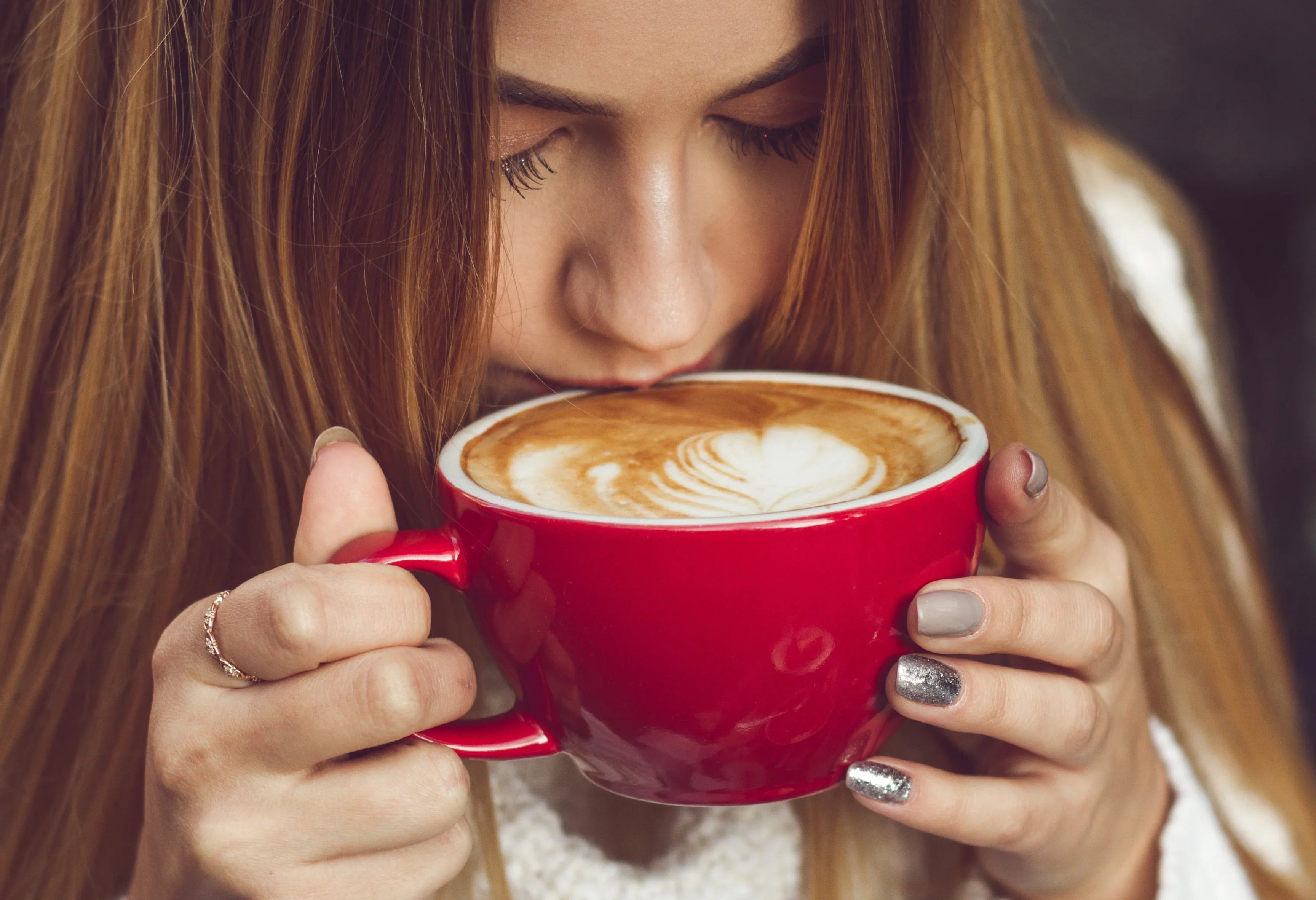 Woman with long hair enjoying latte art coffee in large red mug, cozy setting