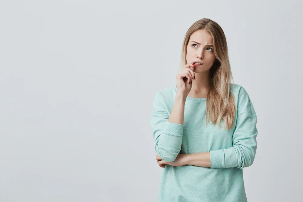 Woman in light blue organic cotton long-sleeve shirt looking thoughtful against plain background