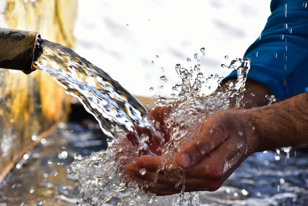Person collecting flowing water from a pipe in cupped hands, clear fresh stream