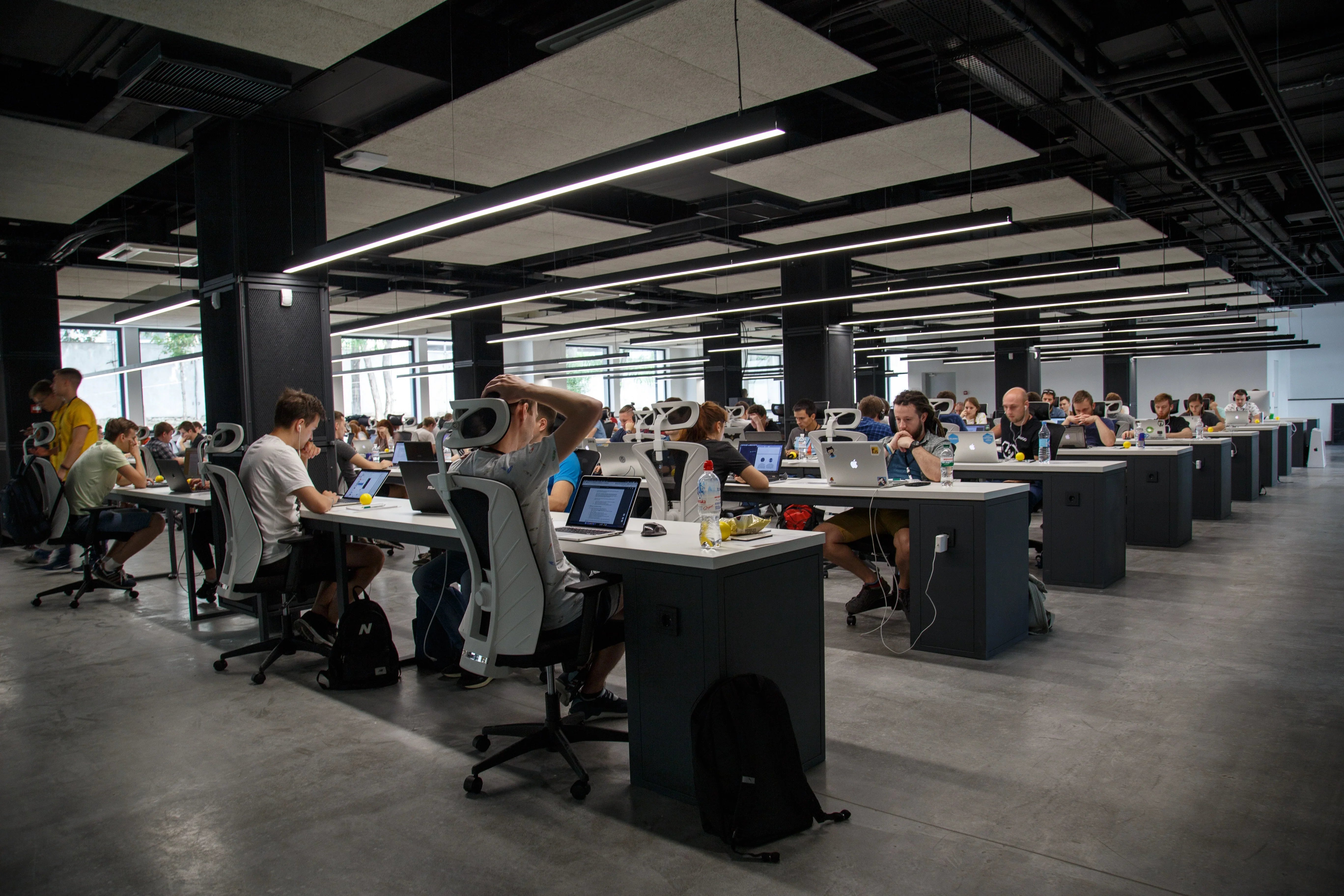 Modern open office with many people working at desks on computers, bright industrial interior.