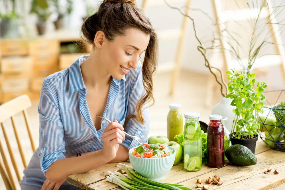 Woman in blue striped shirt enjoying healthy salad with fresh juice and vegetables at table