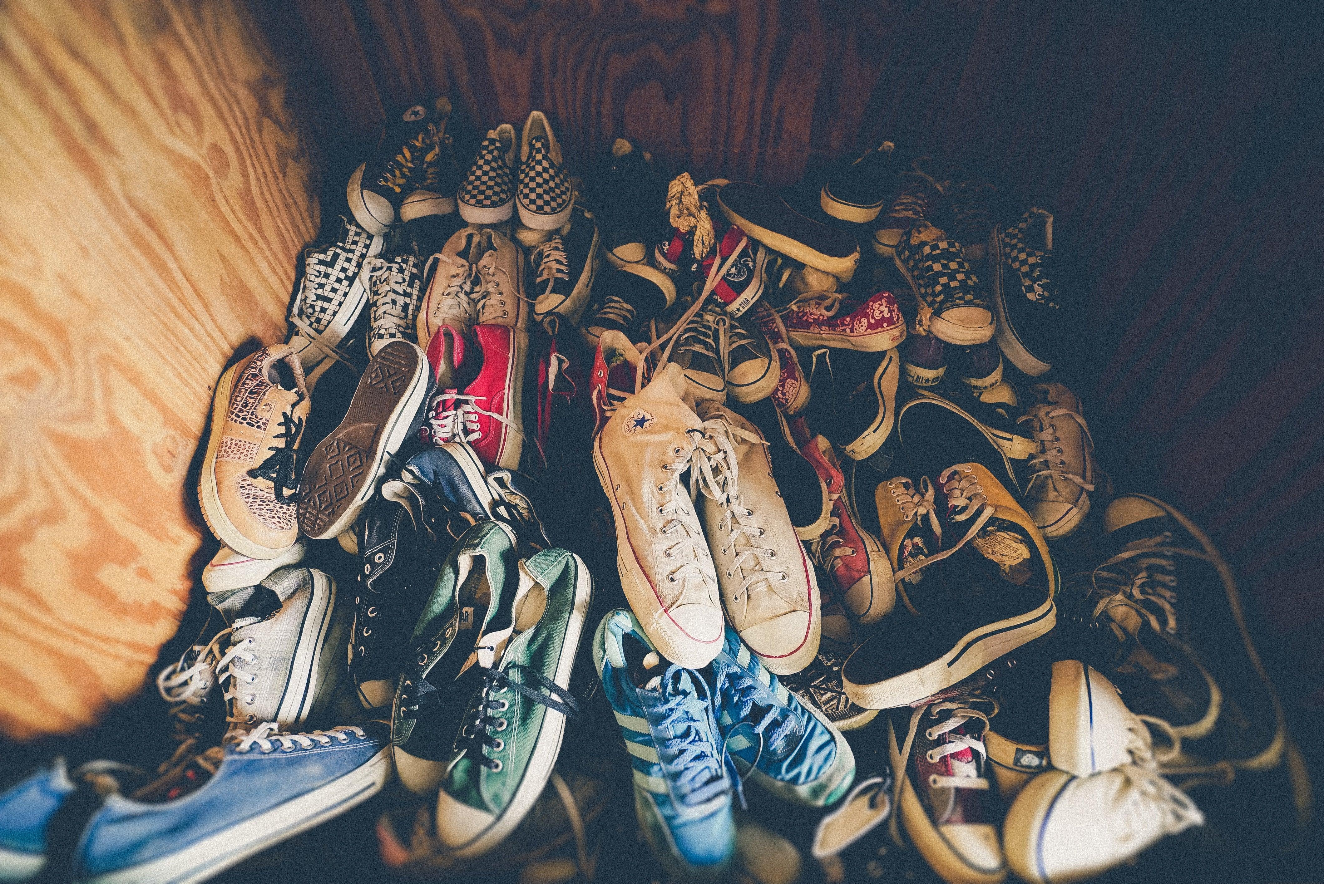 Pile of assorted sneakers and canvas shoes on wooden floor, mix of colors and patterns