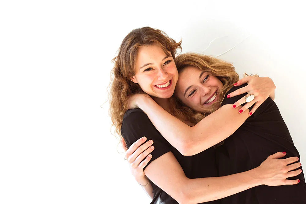 Two women in black allergy-friendly organic cotton shirts hugging and smiling