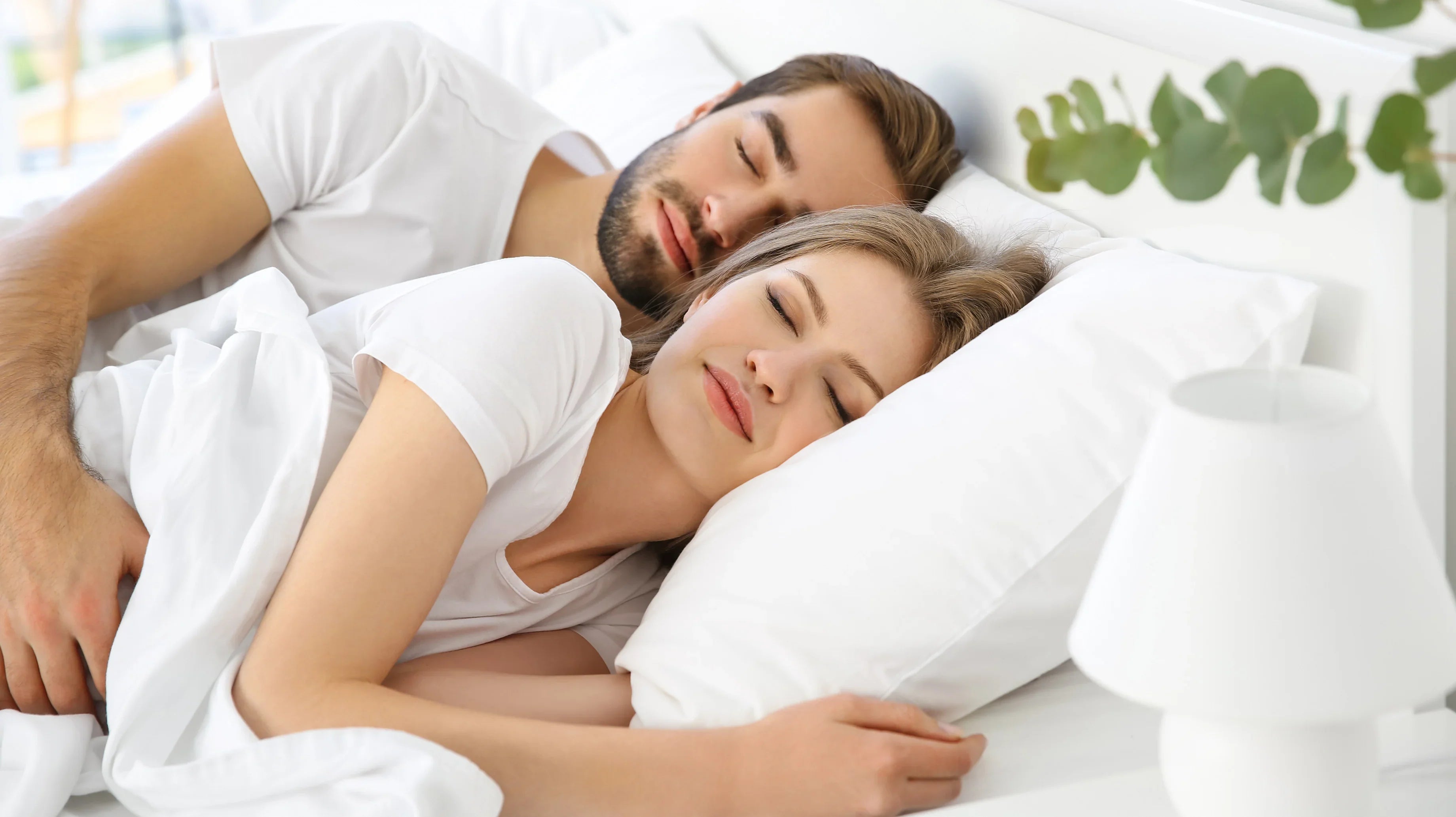 Couple sleeping peacefully in bed, wearing white organic cotton sleepwear for sensitive skin.
