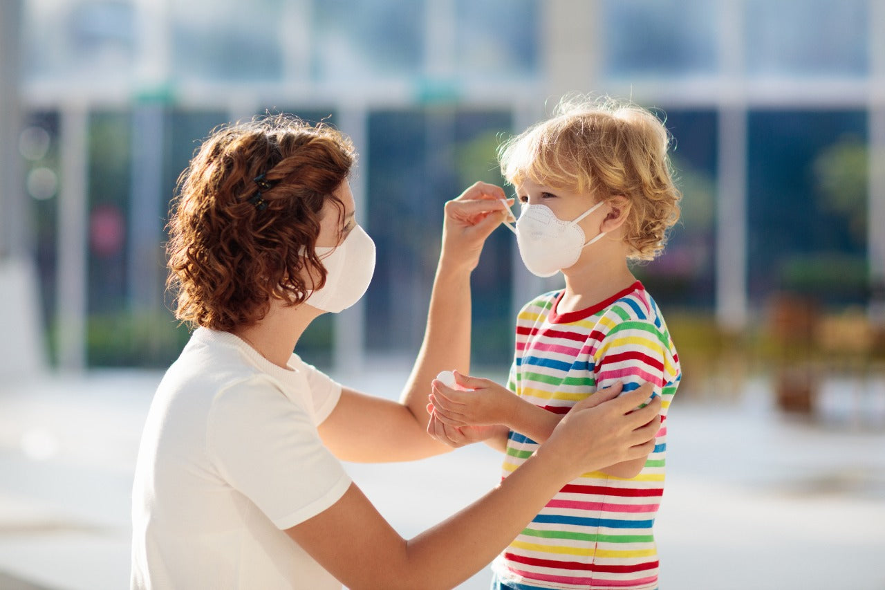 Woman helping child adjust protective cotton face mask indoors