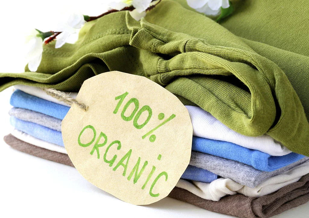 Stack of folded organic cotton clothes with a tag reading 100% organic, in soft pastel colors