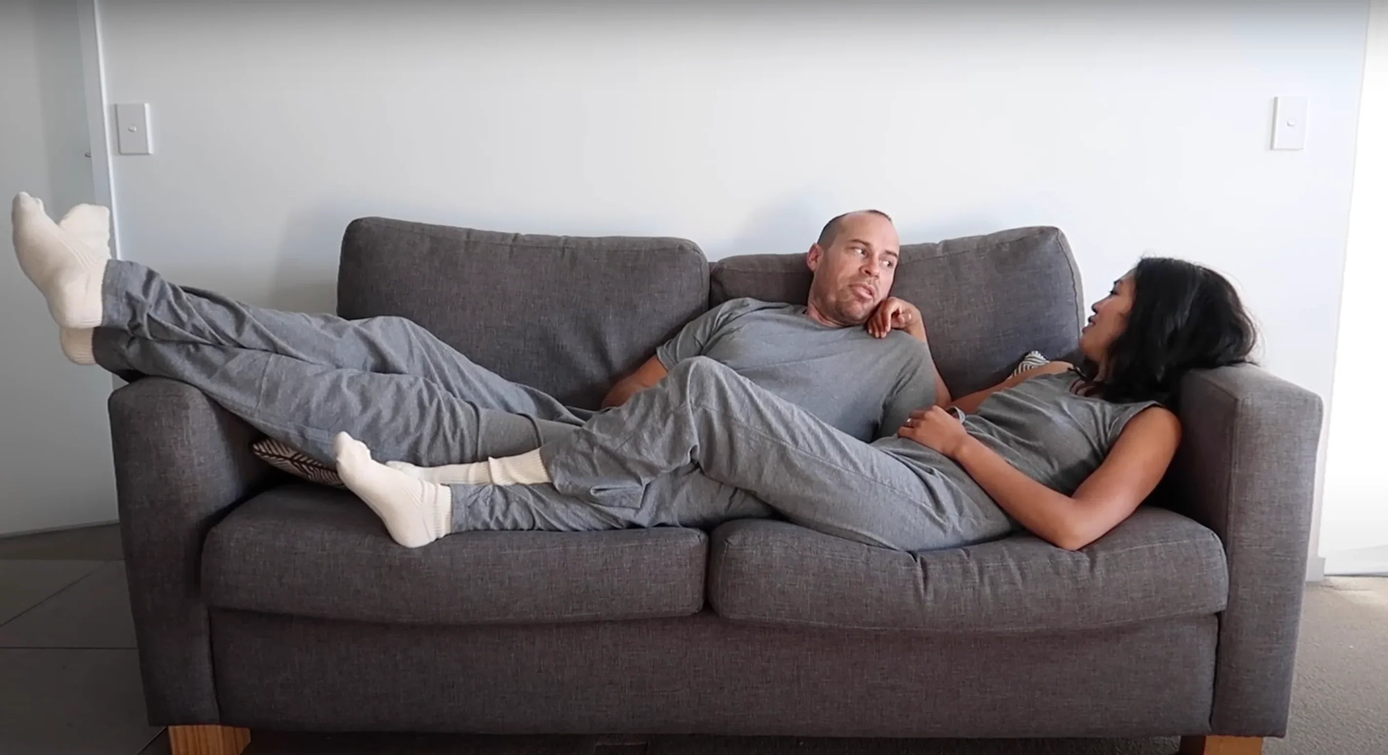 Couple relaxing on grey sofa wearing matching organic cotton loungewear and white socks