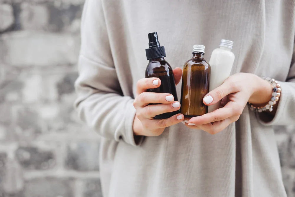 Person in a hypoallergenic cotton top holding three skincare bottles outdoors