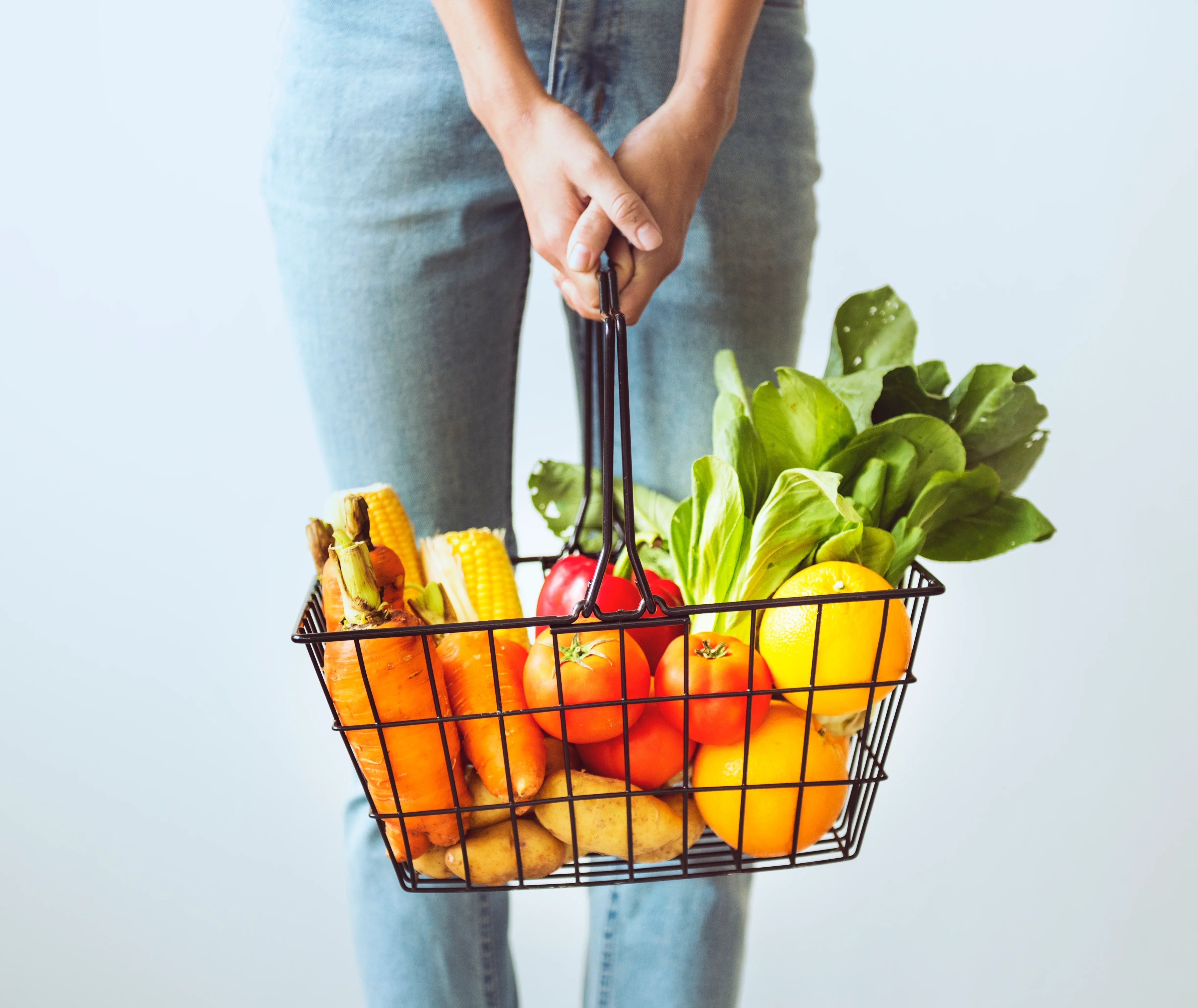 Person holding a basket of fresh vegetables and fruits, allergy-friendly foods