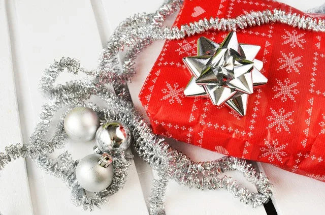 Red Christmas gift box with silver bow, silver garland, and ornaments on white surface
