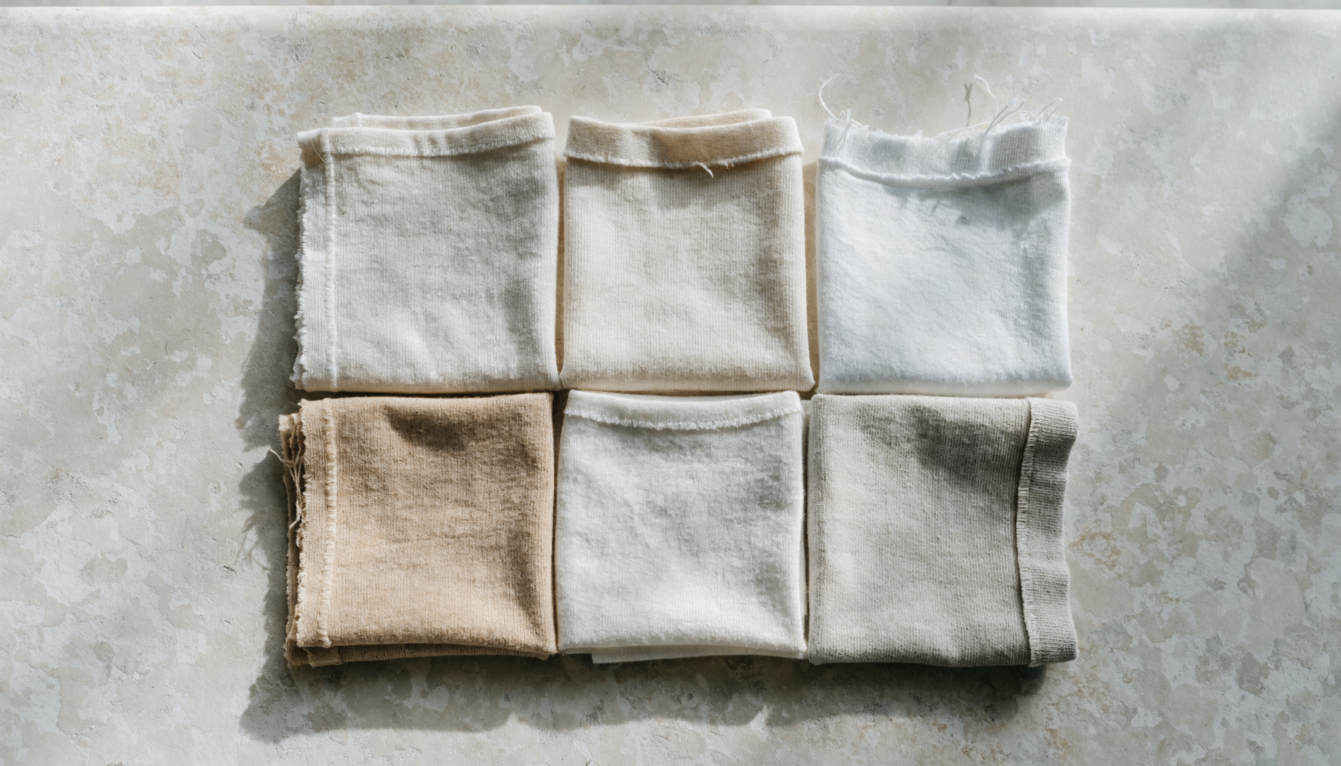 Six folded squares of undyed natural cotton jersey arranged in a grid, each showing a different hem finish