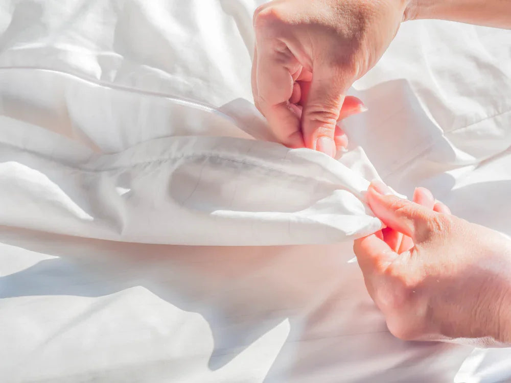 Hands zipping up white organic cotton bedding for sensitive skin
