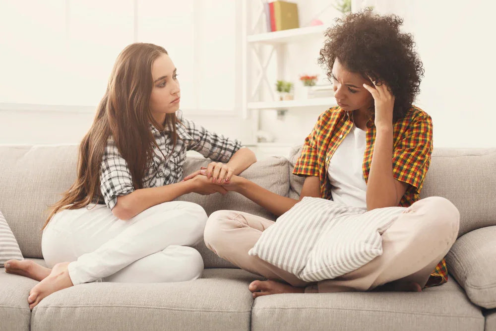 Two women in comfortable cotton clothing sitting on a couch, offering support at home.