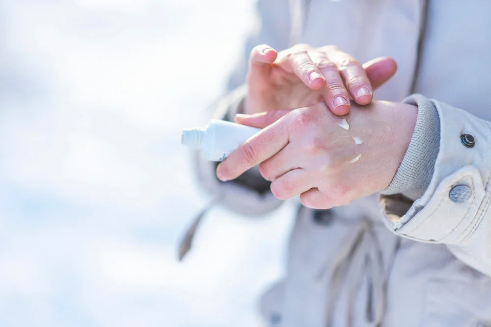 Person applying hypoallergenic lotion to hands outdoors, wearing a light jacket