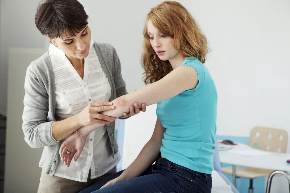 Doctor examining young woman’s arm for skin irritation or eczema in medical office.