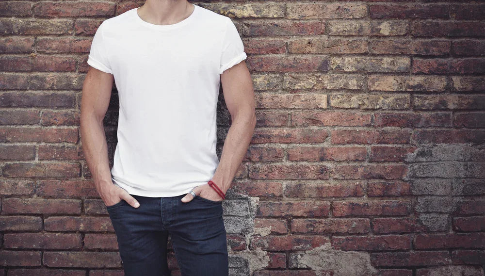 Man wearing plain white organic cotton t-shirt and dark jeans against a brick wall