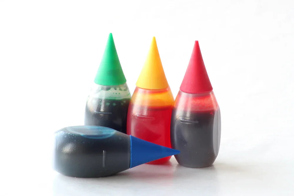 Four small bottles of food coloring in red, yellow, green, and blue on white background
