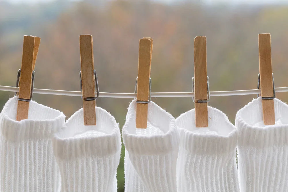 White organic cotton socks drying on a clothesline with wooden clothespins outdoors