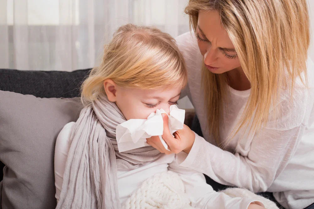 Mother helping child with sensitive skin blow nose, both wearing soft cotton clothes indoors