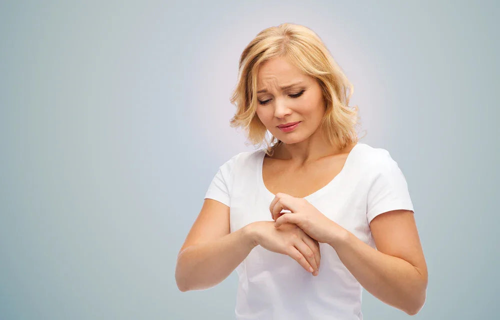 Woman in white shirt scratching her hand, showing allergy discomfort, hypoallergenic apparel