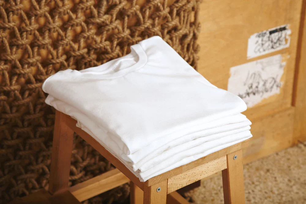 Stack of folded white hypoallergenic cotton shirts on wooden stool