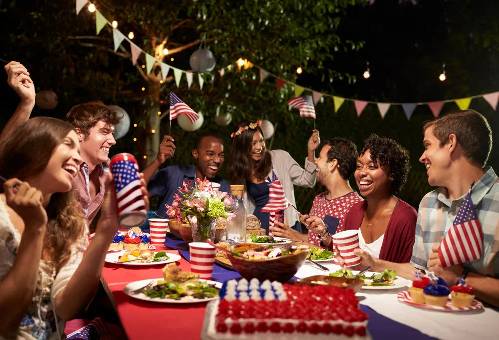 Group of friends celebrating outdoors with American flags, enjoying food at a festive evening party.