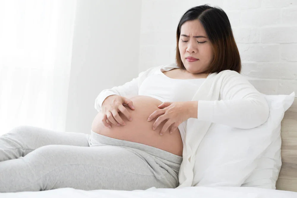 Pregnant woman in allergy-free cotton loungewear scratching belly on bed