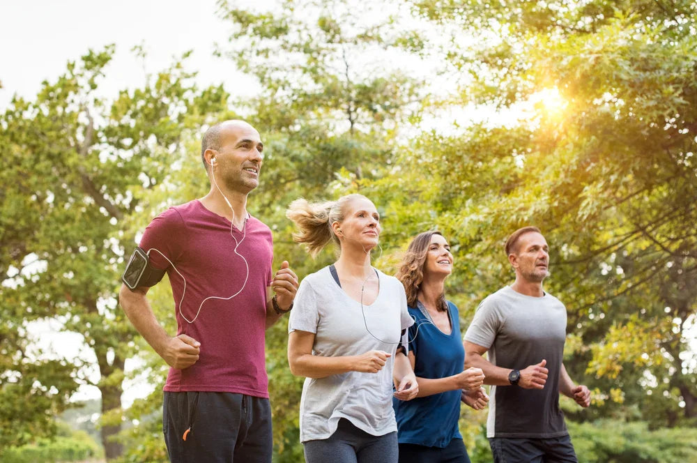 Group of adults jogging outdoors in breathable cotton activewear, sunlight and trees in background