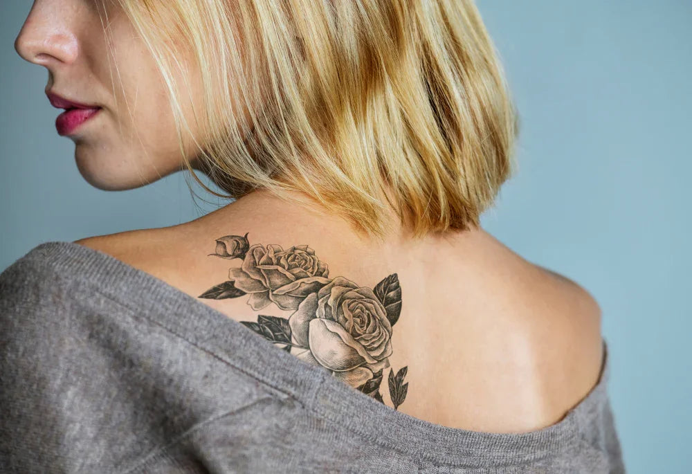 Woman with short blonde hair showing floral tattoo on upper back, wearing a grey shirt