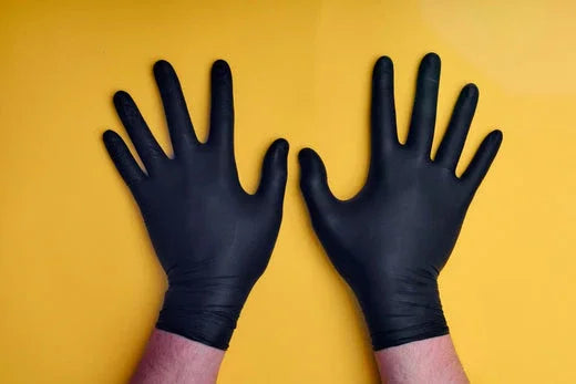 Pair of hands wearing black hypoallergenic gloves on yellow background