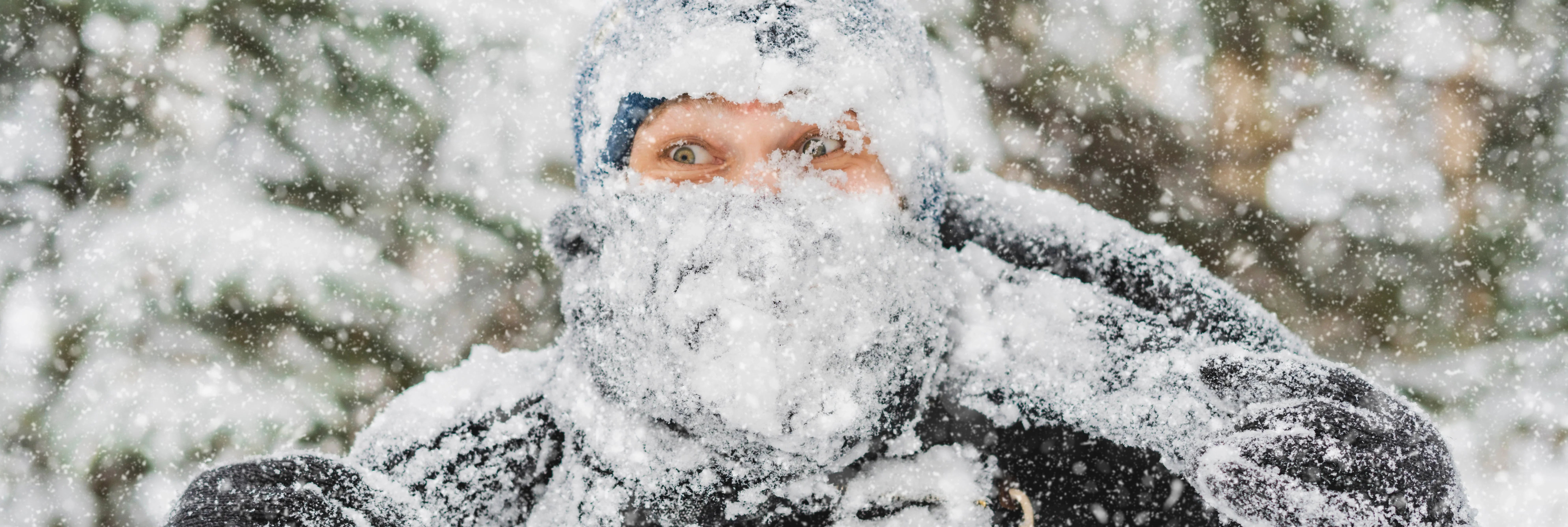 Person bundled in winter clothing, covered in snow, outdoors in heavy snowfall