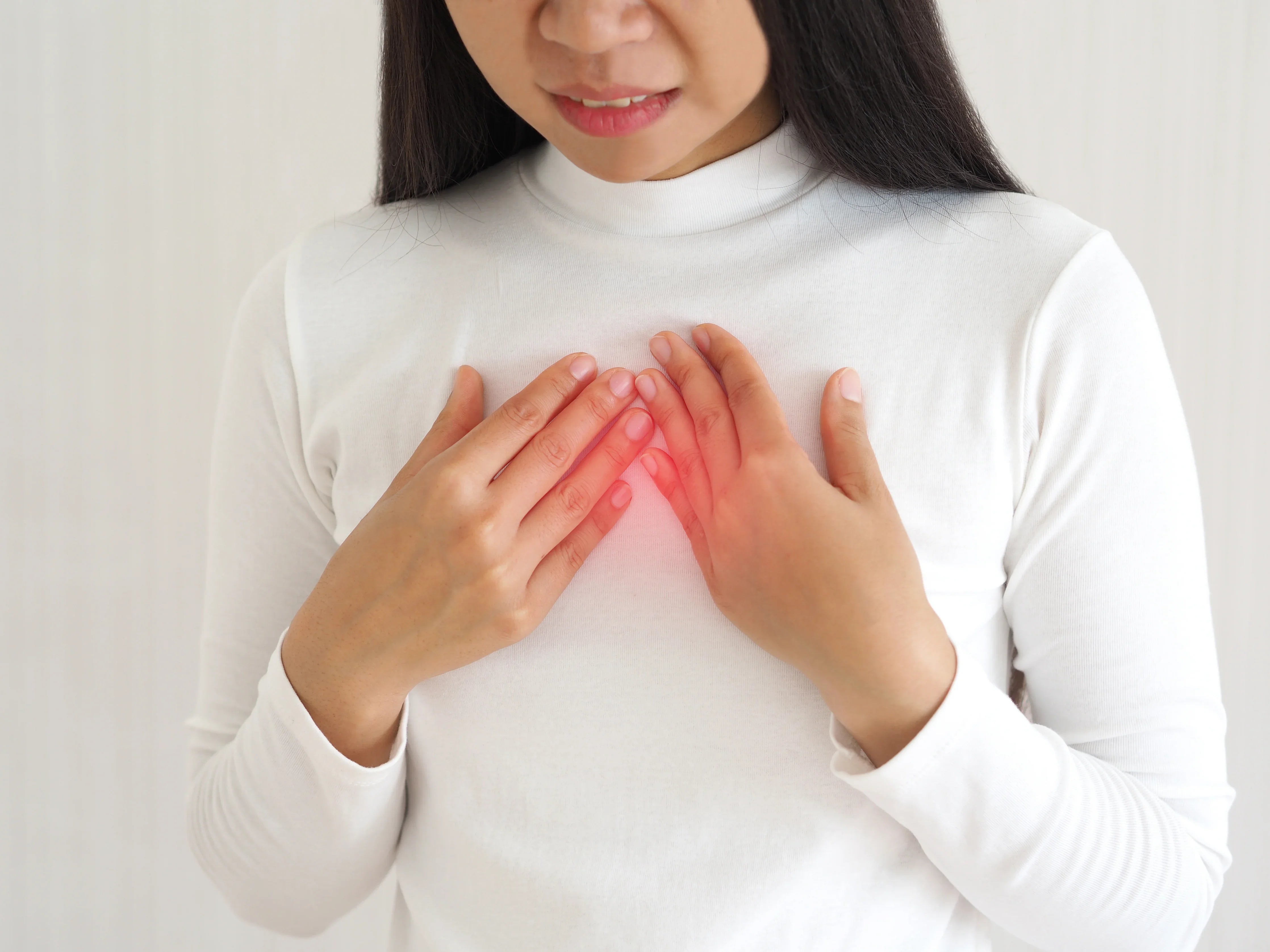 Woman in white shirt touching chest, showing discomfort, allergy-free hypoallergenic clothing