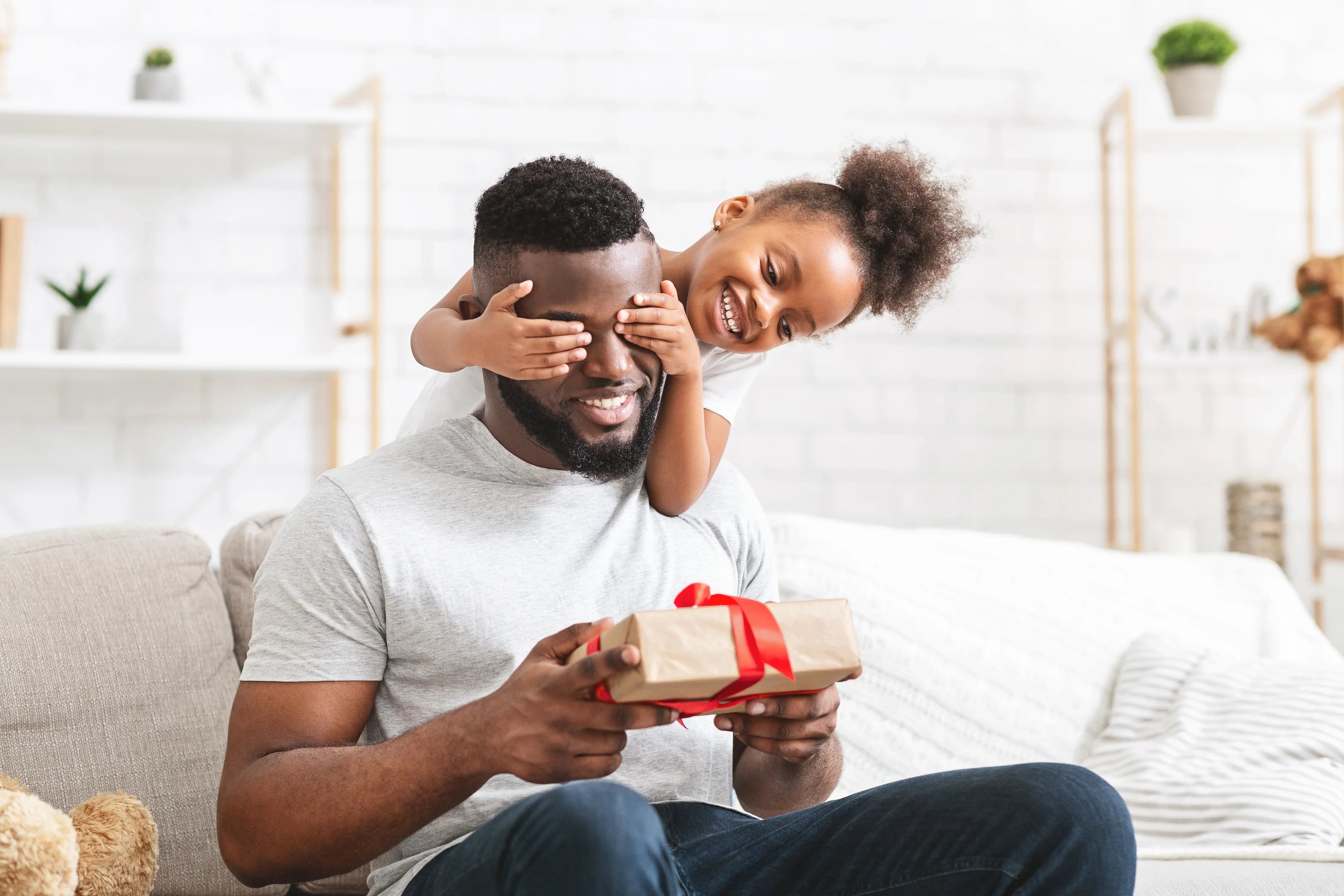 Father and daughter in allergy-free cotton shirts, smiling with a gift, on a sofa