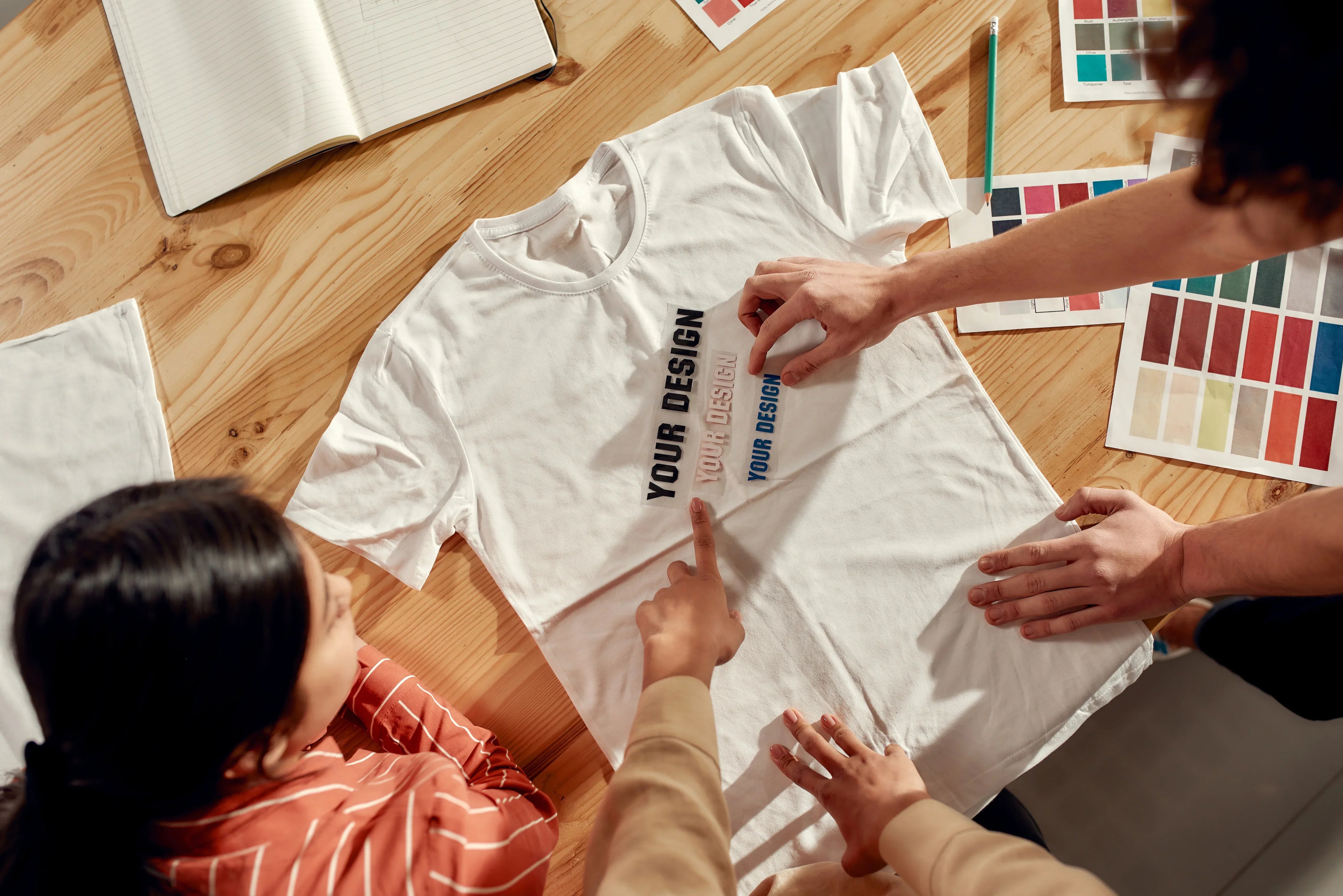 People designing a white hypoallergenic cotton T-shirt with color samples on a desk