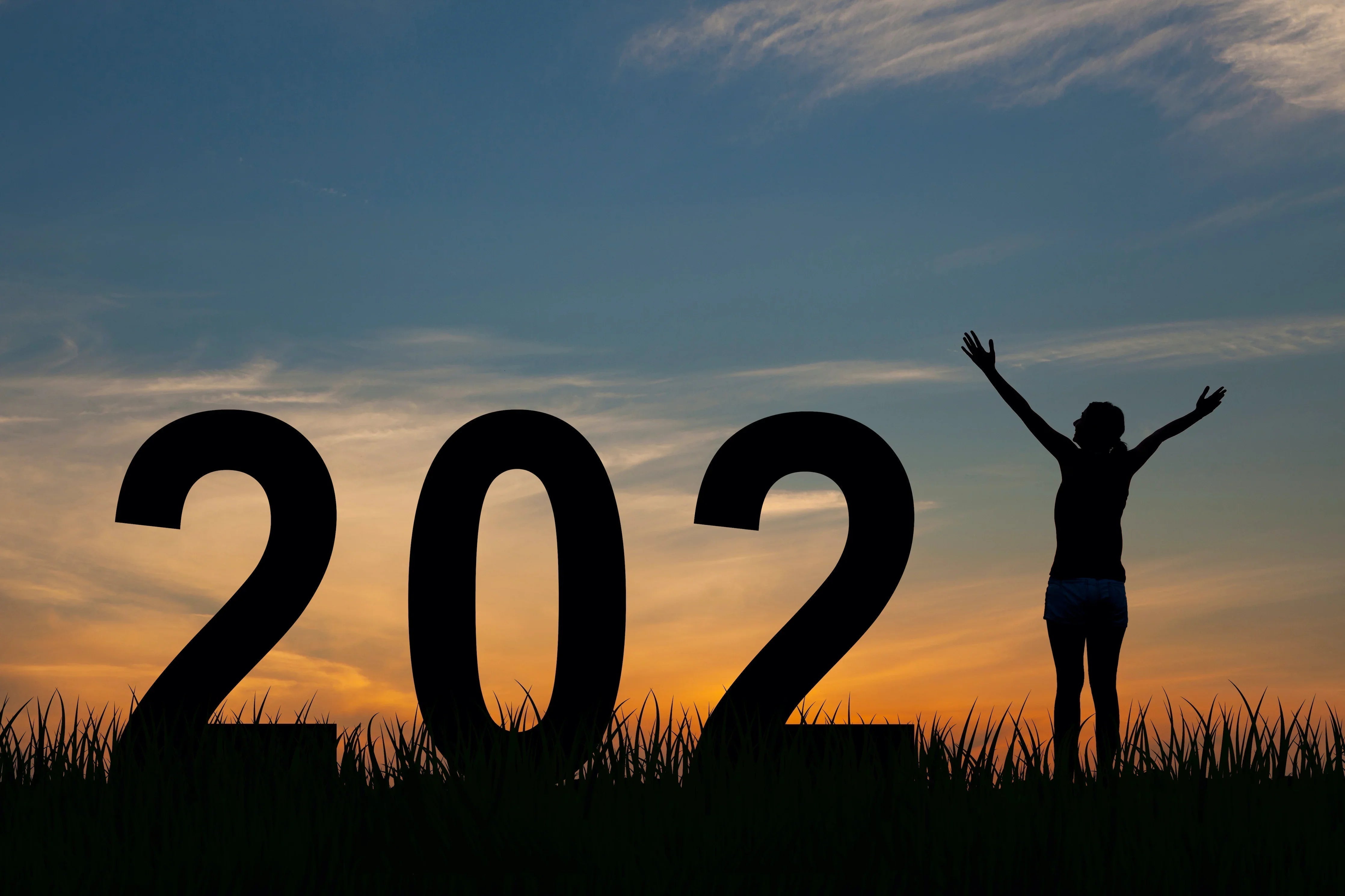 Silhouette of a person celebrating next to large 2022 numbers at sunset outdoors