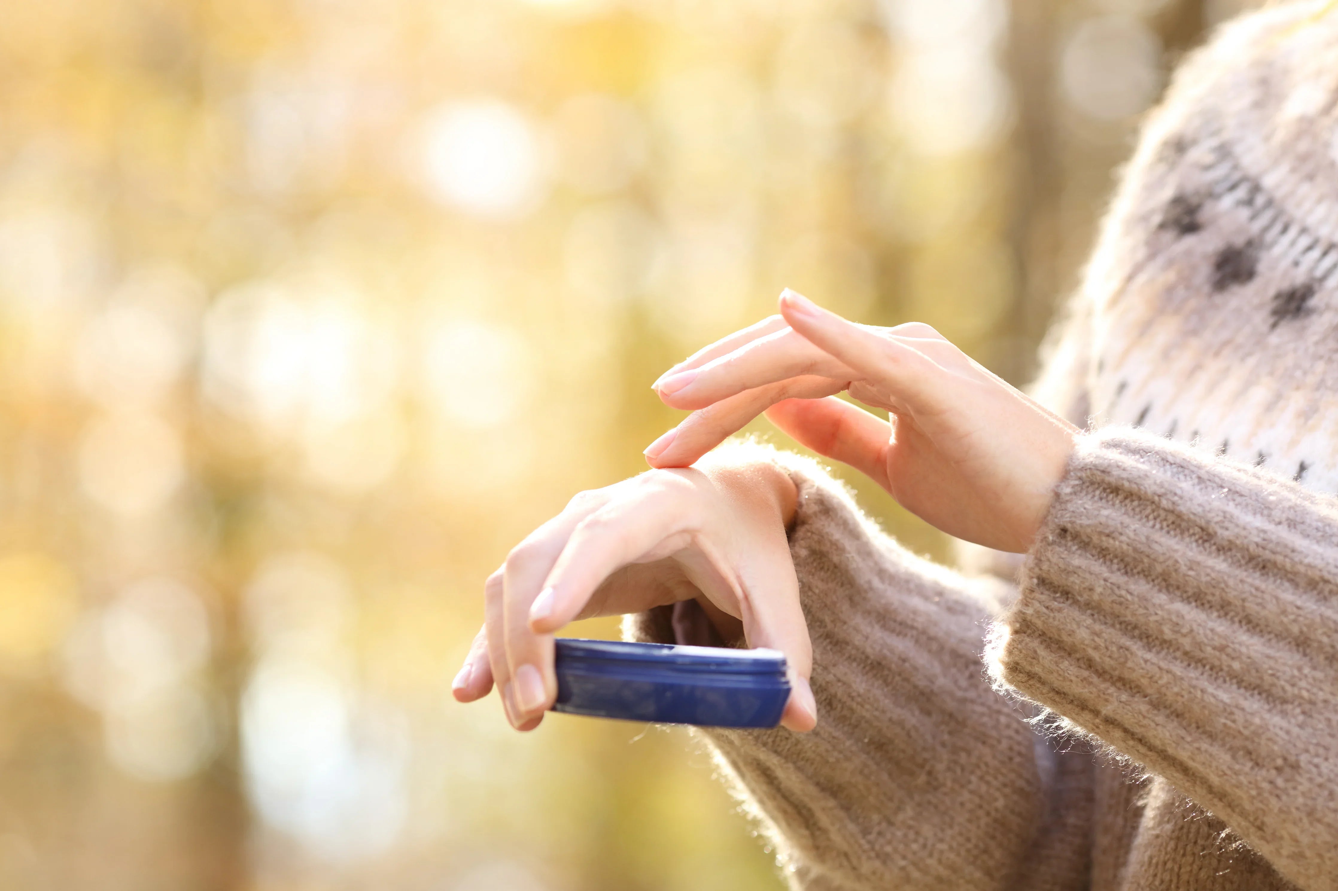 Person applying moisturizing cream on hand for sensitive skin, wearing soft knit sweater