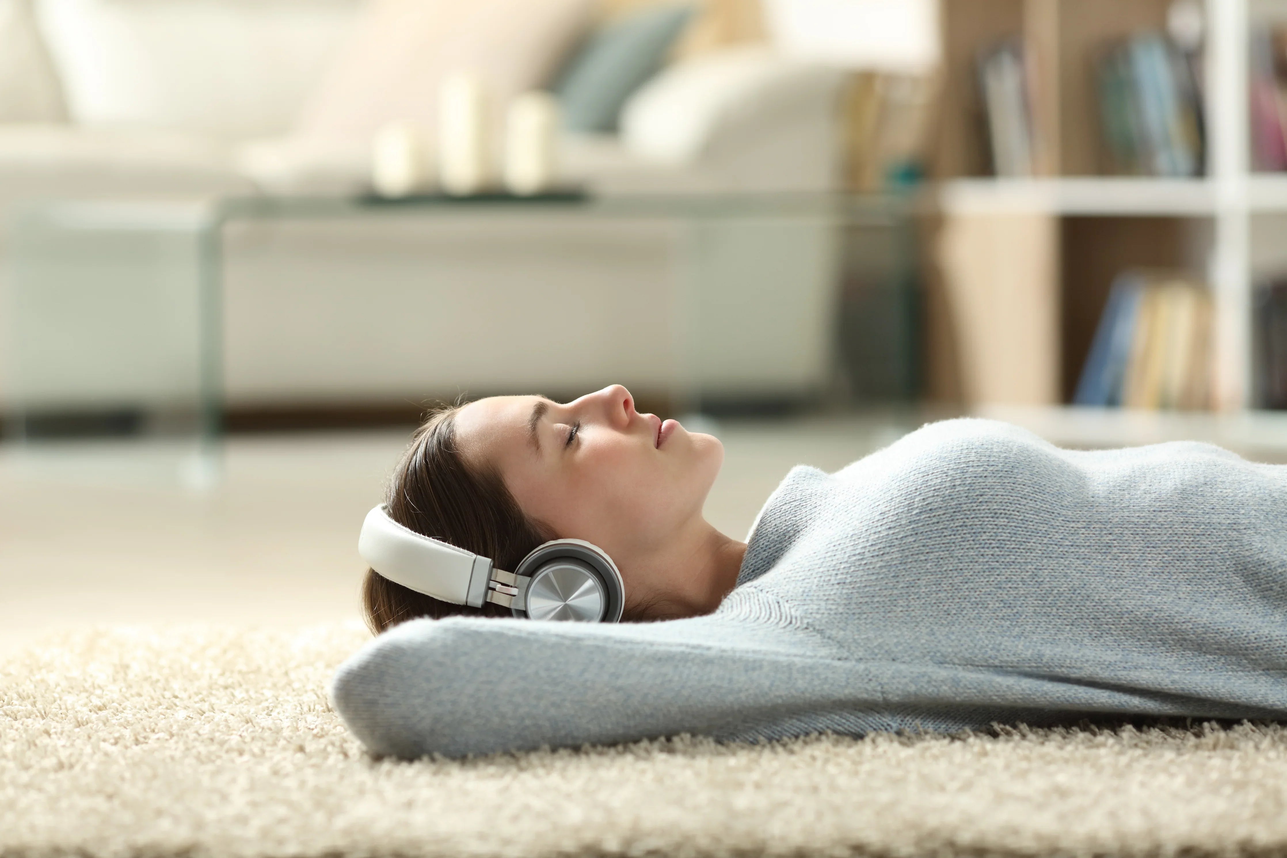 Woman relaxing on carpet in cozy sweater, wearing headphones, in a modern living room