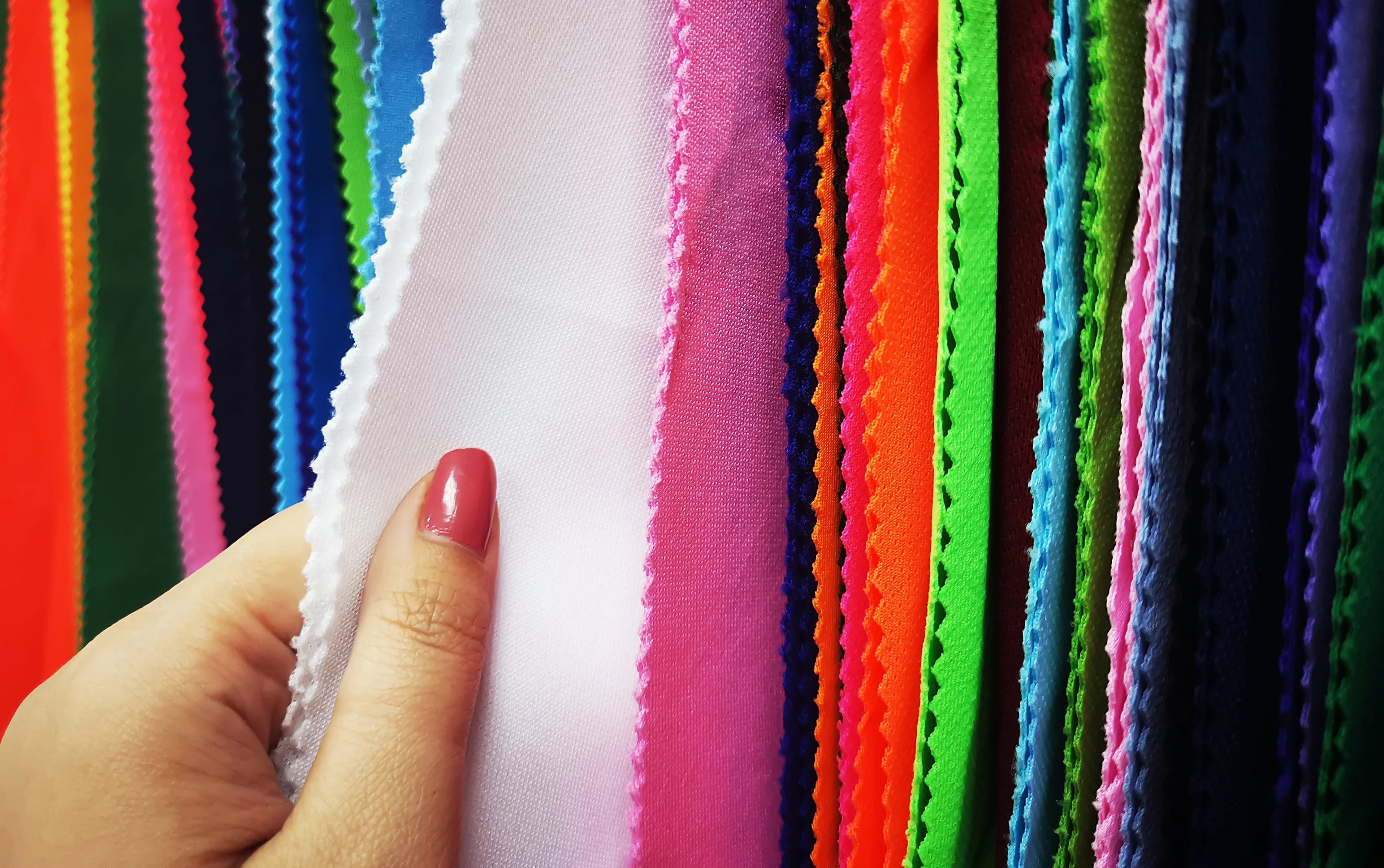 Hand touching assorted colorful allergy-free cotton fabric swatches, Cottonique clothing.