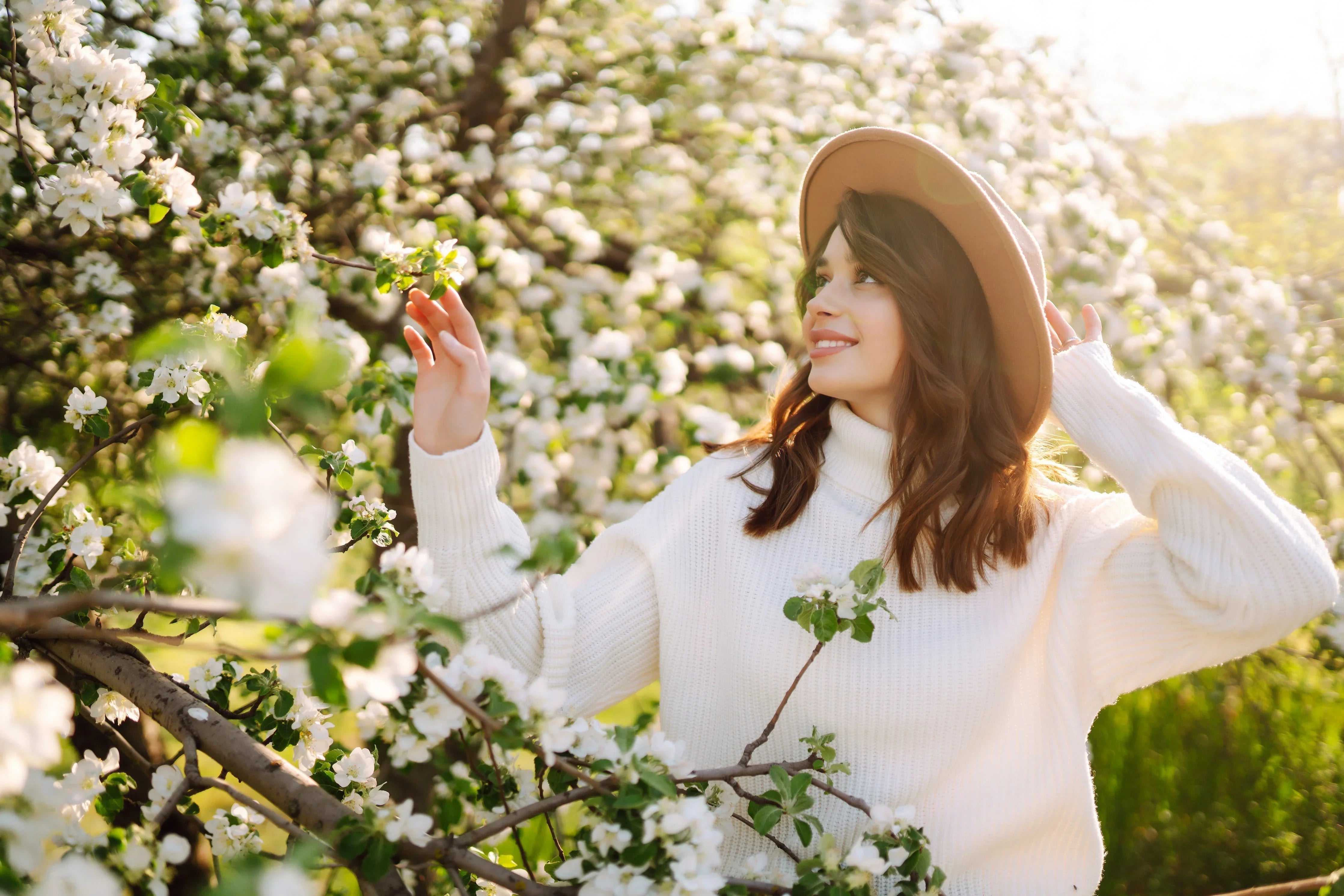 Woman in a white cotton sweater and hat among blooming spring flowers outdoors