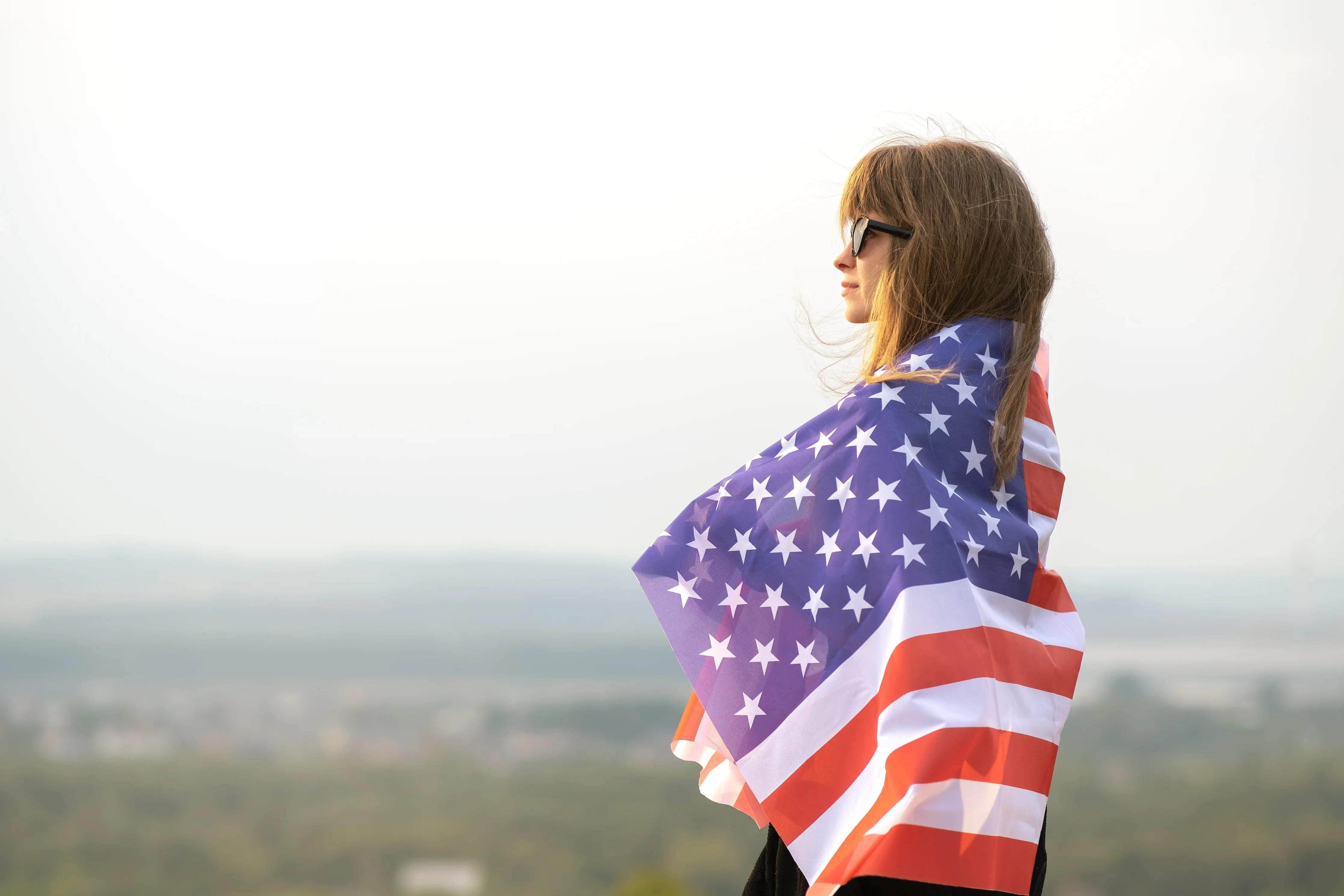 Woman wearing sunglasses wrapped in American flag, outdoors with blurred background