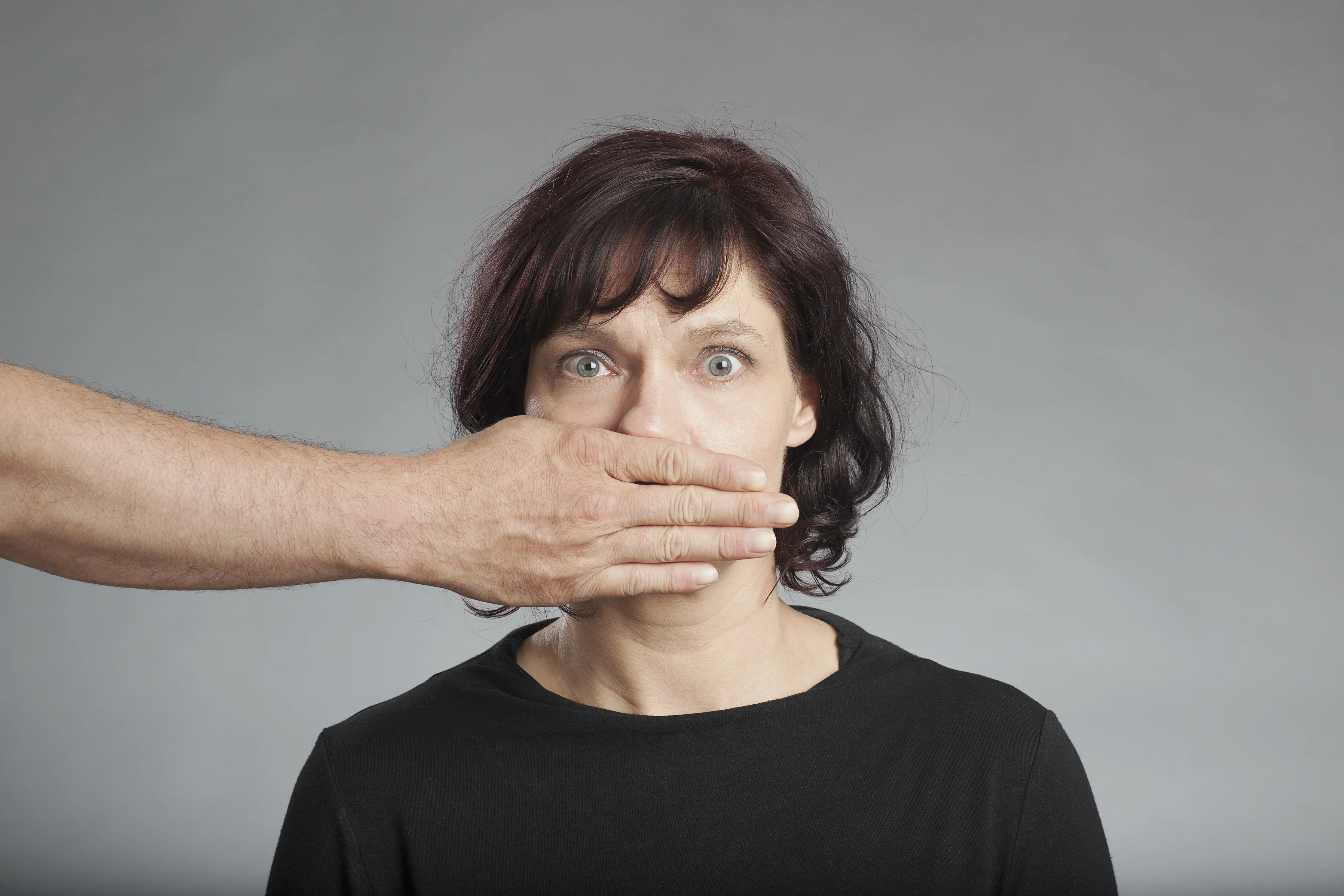 Woman in black shirt with a hand covering her mouth, neutral gray background
