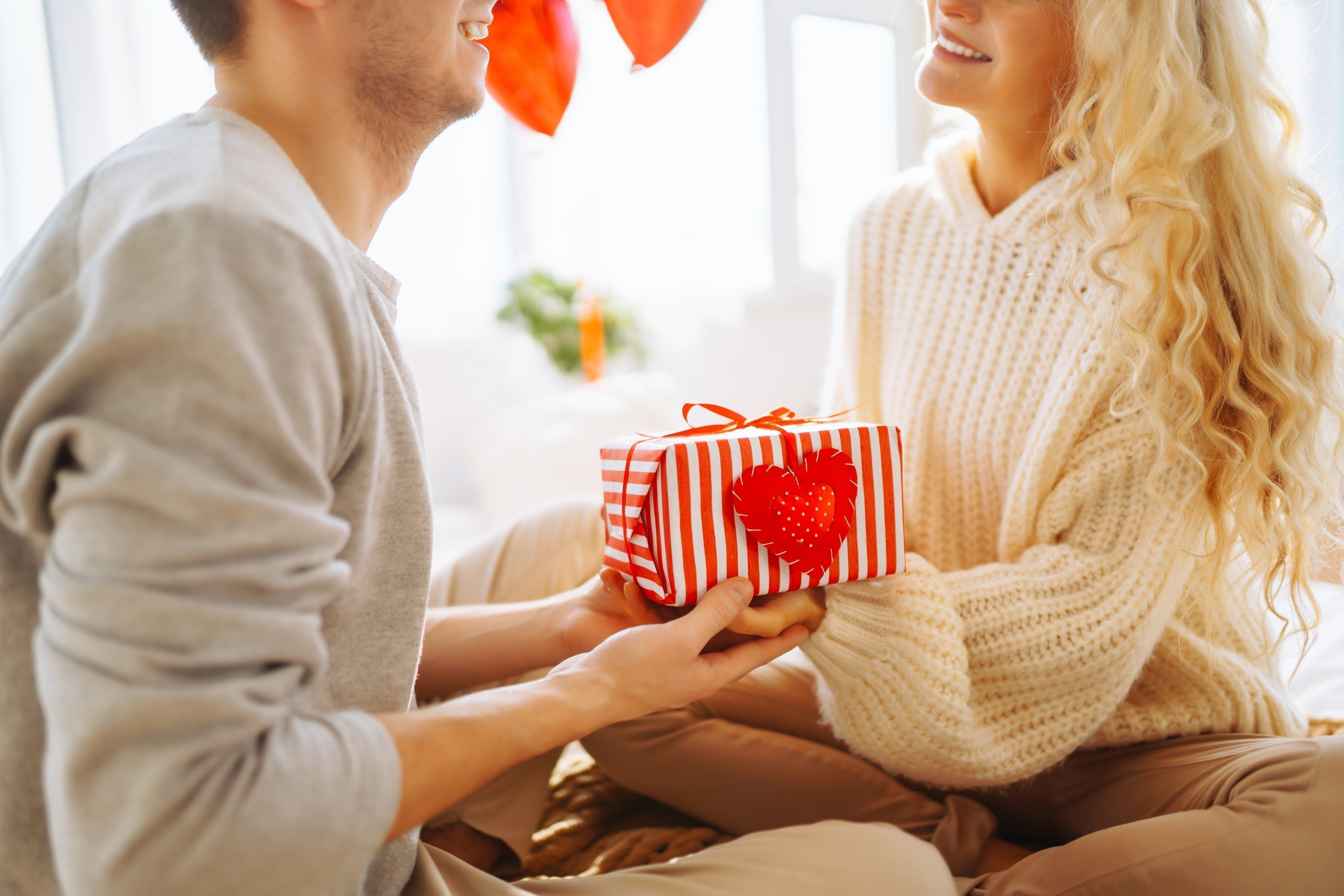 Smiling couple exchanging a striped gift box with heart, wearing cozy knit allergy-free apparel.