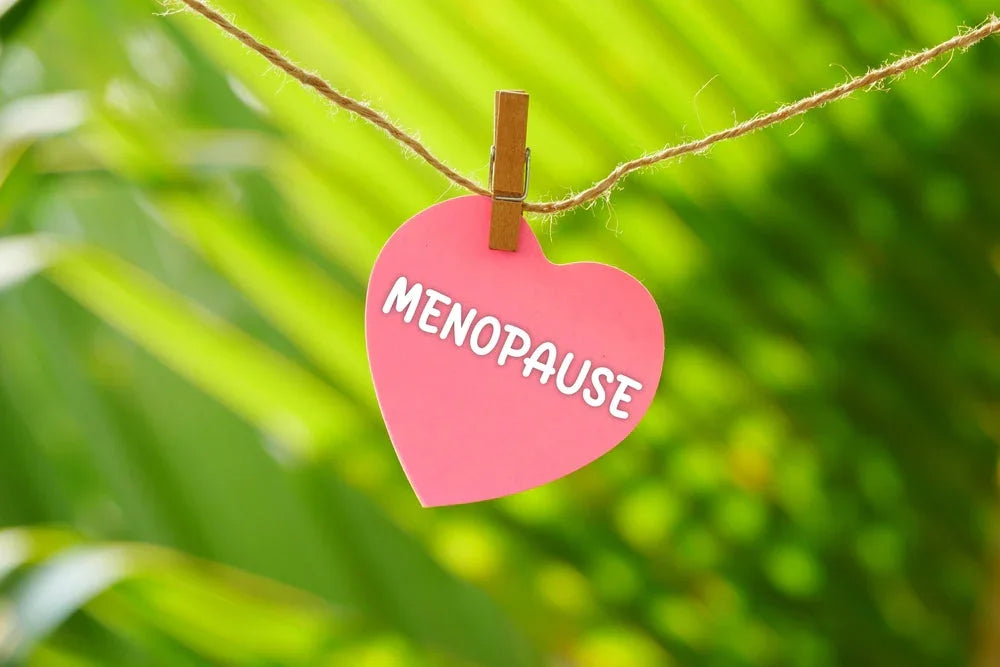 Pink heart-shaped menopause sign hanging on clothesline with green nature background