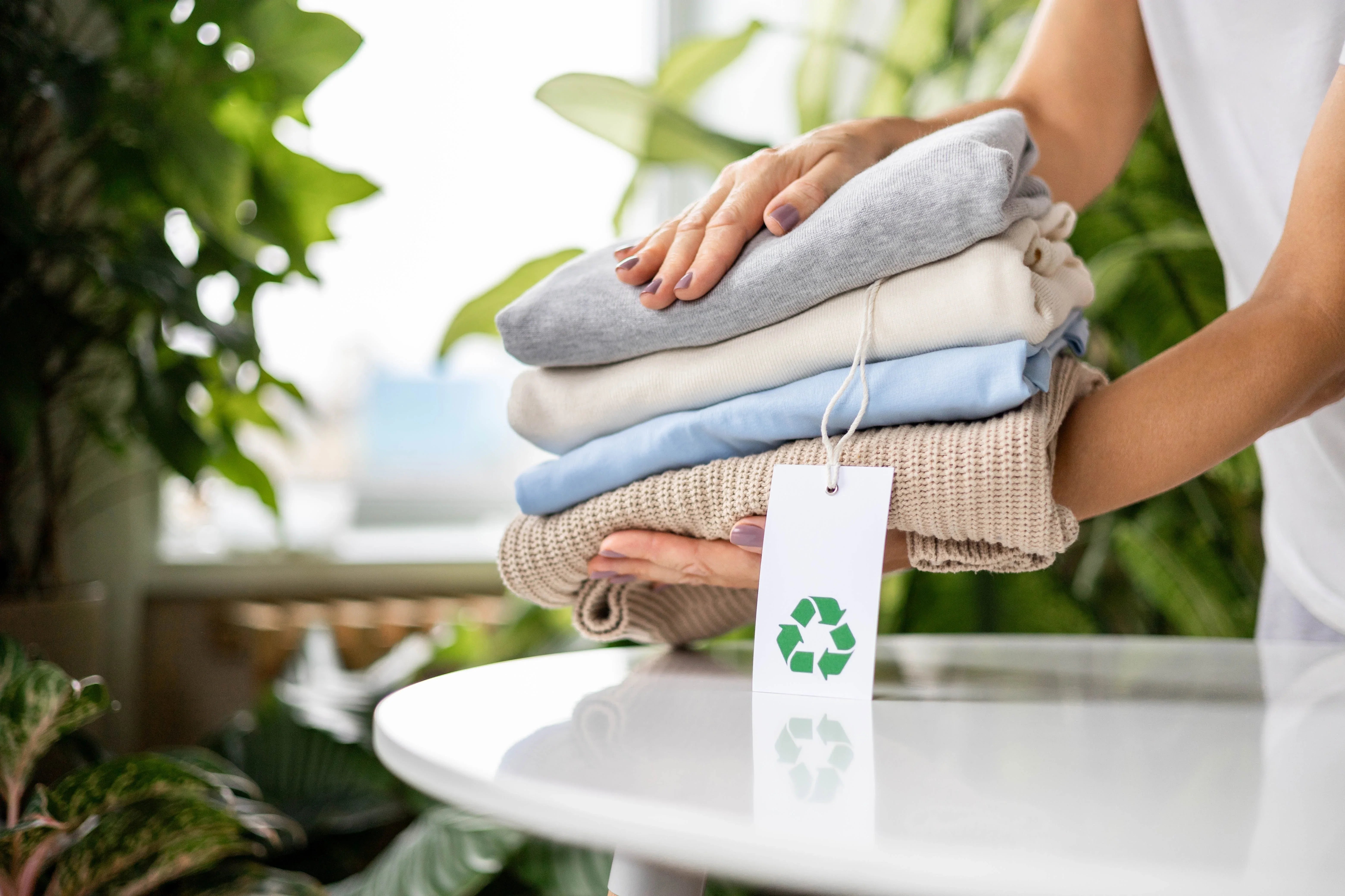 Person holding folded organic cotton clothes with a recycling tag in a bright room